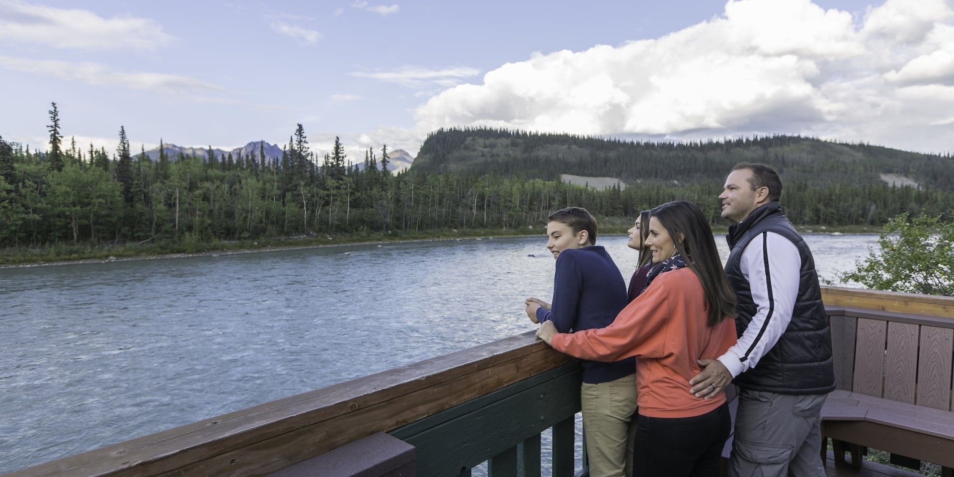 A family looks out at a lake in Alaska from an overlook.